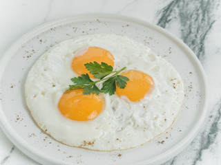 Breakfast is three eggs fried on a white plate on a white marble background. Decorated with parsley. Scrambled eggs with cheese. Photo for the menu.