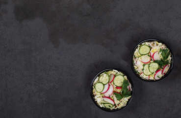 Vitamin salad of fresh vegetables cabbage, radishes, cucumbers and parsley in a bowl on a dark background top view