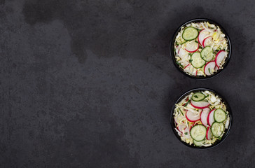 Vegan salad with fresh cabbage, radish, cucumber and parsley in a bowl on a dark gray background top view