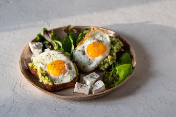 Healthy breakfast- sandwich prepared with guacamole, pepper and fried eggs with feta cheese and avocado on grey background