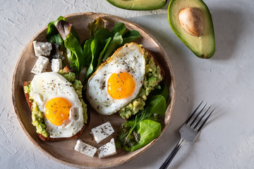 Healthy breakfast- sandwich prepared with guacamole, pepper and fried eggs with feta cheese and avocado on grey background
