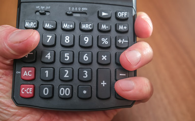 Close up of human hand holding a black calculator with selective and close focus on the number pad