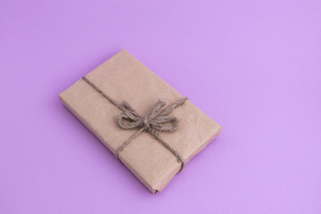 Gift in eco-friendly packaging made of craft, recycled paper on a light, lilac background.