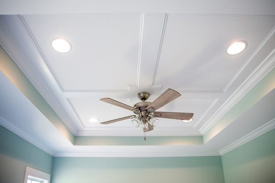 White tray master bedroom ceiling in small new construction house with windows and a ceiling fan and pale blue turquoise walls
