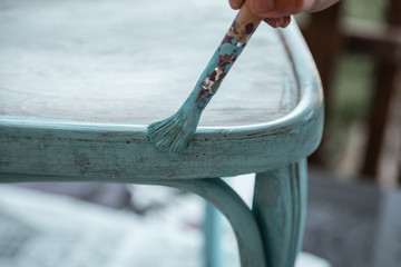 Middle-aged woman's hand with brush restores a wooden chair with turquoise paint
