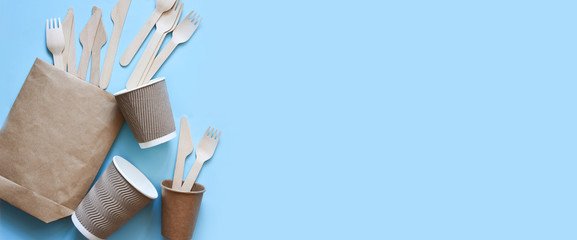 Disposable eco-paper dishes: glass, cardboard, bag, fork, knife. On an empty blue background. The layout of wooden cutlery on a blue background.