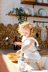 Little girl sit on the kitchen table and cook Breakfast, have fun laughing play in the kitchen at home. Kitchen in a rustic style. Eco kitchen.