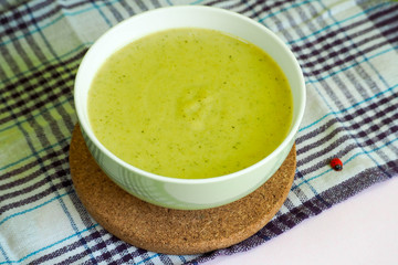 broccoli zucchini onion and potato puree soup with cream in a white bowl on a lilac-striped towel and a wooden stand on a light table . decor ladybug . gluten-free food and diet .cooking at home