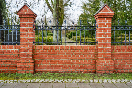 Beschaffenheit einer roten Ziegelsteinmauer mit grauen Zementfugen zwei Säulen und einem schmiedeeisernen Zaun