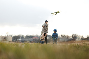 Young mother with two children, a little girl and a boy playing in the autumn field. Autumn family in the Park playing with toy airplane.