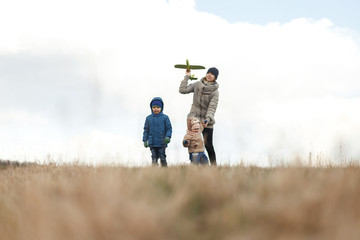 Young mother with two children, a little girl and a boy playing in the autumn field. Autumn family in the Park playing with toy airplane.