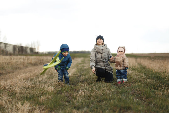 Young mother with two children, a little girl and a boy playing in the autumn field. Autumn family in the Park playing with toy airplane. - Powered by Adobe