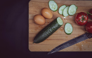 Top view of fresh vegetables, chicken eggs and a knife. One cucumber, tomatoes on a branch