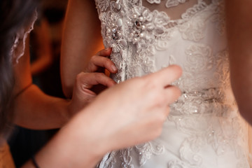 the bride in the wedding dress is standing with her back.The girlfriend ties the lace on the dress .Her hands close up
