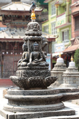 One of many stone buddhist statues of sitting Buddha in Kathmandu city, Nepal. Pigeon sits on top of monument. Religious architecture theme.