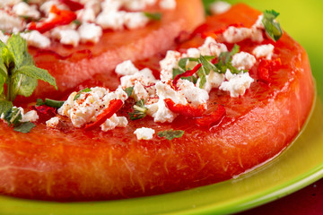 Grilled watermelon with feta cheese, chili pepper and min on green plate on red background. BBQ healthy food concept.