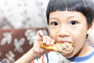 Hungry asia little boy eating chicken leg. Child hand holding a fried chicken.