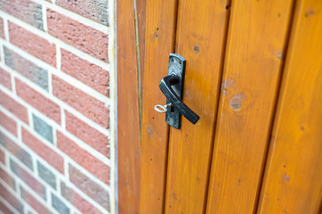 Closed wooden garden door with key inside with black handle, visible red brick wall.