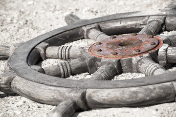 Close up of an old ships wheel laying in the sand.  Finished in black and white with the rusted center of the wheel colorized to add dimension.