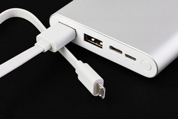 An additional stand-alone power bank for charging mobile devices. External battery on a black background. White charger for smartphone, power supply (battery bank). Full depth of field.