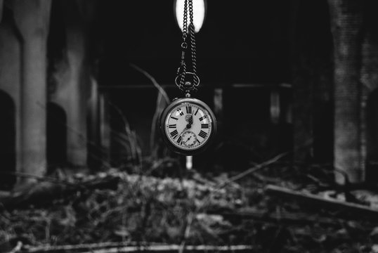 Antique watch with chainlet hanging over heap of bricks and wood in an abandone catholic church. Creepy concept of time. Black and white.
