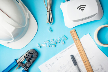 Tools for installation of wireless networks and structured cabling. Internet and data network design service. Engineer helmet, network cable, modem, utp terminals on blue background.