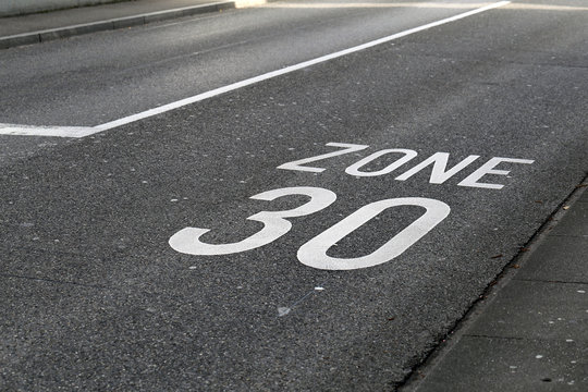 Asphalt driveway in Switzerland with 30km/h speed limit. Speed limit marked to road with text "zone 30". Urban area in a Swiss city. Color image with no people.