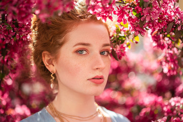 Young beautiful redhead girl with natural freckled skin posing in blooming garden. Outdoor close up portrait. Copy, empty space for text