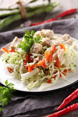 Healthy food. Fresh salad from cabbage, pepper and herbs with chicken on a white plate. Bean pods, chili peppers and parsley on a grey wooden background. Rustic. Background image, copy space