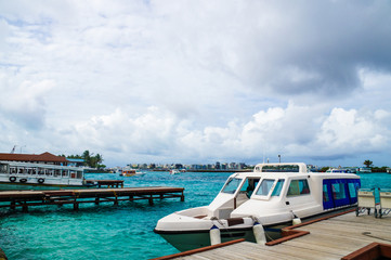 The pier on the island with white boat. Azure water in port. Maldives islands transport.