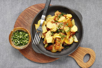 Fried potatoes in a cast iron pan on a gray background