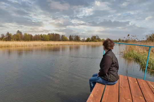 Woman facing at river while sitting on wooden pavement