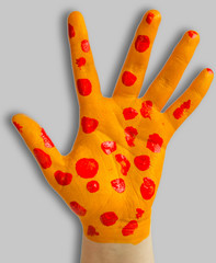 A close up of a human hand painted yellow with bright red spots on a white background isolated