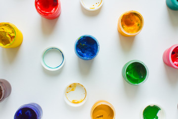 Multi-colored paints-plastic jars of gouache on a white paper background top view