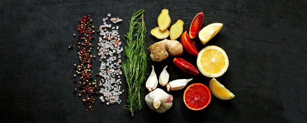 Fototapeta na wymiar Selective focus. Set spice on a black stone board. Peppers mix, Himalayan salt, rosemary, garlic, lemon, ginger, red orange. Spices for fish or meat. Spices for marinade. Spices for a healthy diet.