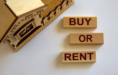 Wooden blocks form the words 'buy or rent' near miniature house.