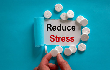 The text Reduce Stress appearing behind torn blue paper. White pills and male hand.
