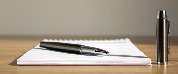 White notebook pen and cap on beautiful wood table. Warm sunlight.