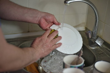 A man washes dishes with his hands with water from the tap.