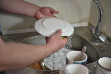 A man washes dishes with his hands with water from the tap.
