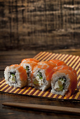 Sushi on a white plate. Sushi roll with sauce and spices on a black background. Food on a wooden table with dark boards. Place for text near land.