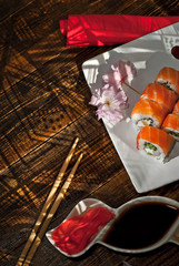 Sushi on a white plate. Sushi roll with sauce and spices on a black background. Food on a wooden table with dark boards. Sakura color on a plate. Flower with rose petals.