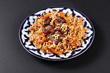 Plov pilaf plate on black background. Traditional Uzbek cuisine.