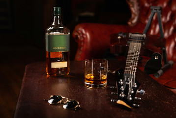 A bottle of Irish whiskey, with a glass, glasses, and a guitar on the table. Place for text or logo. - Powered by Adobe