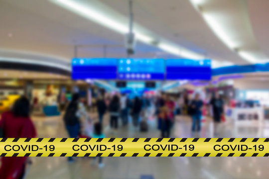 Covid-19 warning tape with blurred airport image on the background. Coronavirus spread and restrictions concept