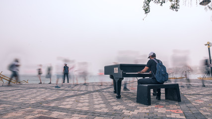 Blurred Motion Of People Walking In City with Young man playing the piano 