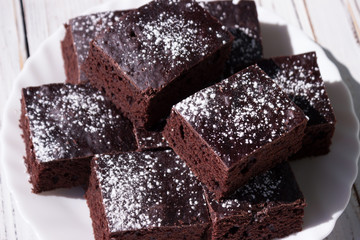 Chocolate cake cut into square pieces, sprinkled with icing sugar on a plate, white background
