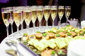 crystal champagne glasses stand on a serving table and in front different snacks for guests
