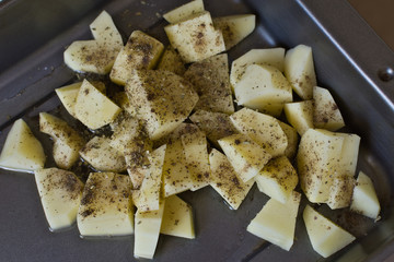 Raw potatoes sprinkled with herbs prepared for baking