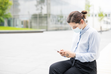 Frau mit Smpartphone macht Pause vor Bürogebäude auf Campus oder Technologiepark. 